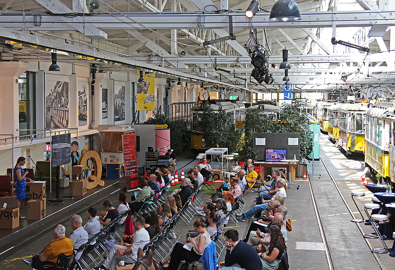 Menschen sitzen in der Stuhlreihe mit alten Straßenbahnen im Hintergrund